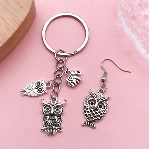 Porte-clés hibou en argent antique et boucles d'oreilles sur un fond rose pastel