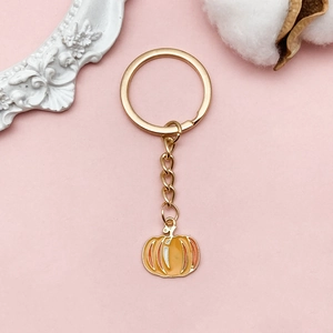 Cute golden pumpkin pendant keychain with orange enamel finish on decorative background