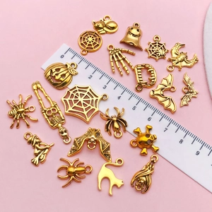 Detail of assorted golden Halloween alloy charms including pumpkins and bats on pink background