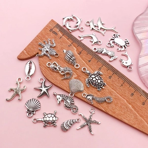 Tibetan silver ocean charms including starfish and turtles on pink background with caliper