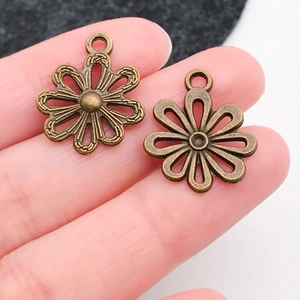 Detailed view of two vintage bronze alloy sunflower pendants held in hand for DIY jewelry