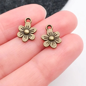 Macro shot of vintage bronze flower charms on a finger showing realistic size and texture