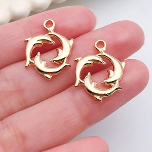 Vue détaillée de deux breloques dauphins dorées tenues en main pour bijoux artisanaux