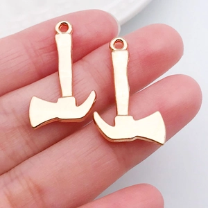 Makroaufnahme von roségoldenen Axt-Anhängern für DIY-Schmuck auf einer Hand zur Größenansicht