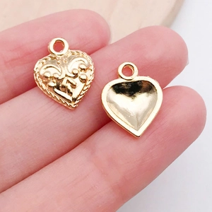 Macro shot of gold heart charms showing intricate floral relief and smooth back for DIY