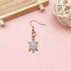 Macro detail of a golden sea turtle enamel earring with floral patterns on a pink background