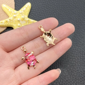 Detailed macro view of pink enamel sea turtle alloy pendants held by hand for DIY jewelry