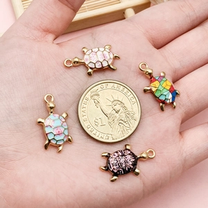 Set of 4 turtle alloy charms with colorful floral enamel patterns next to a coin