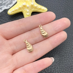 Détail de deux breloques coquillages dorées pour colliers DIY tenues en main