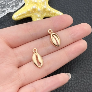 Gros plan de pendentifs coquillage dorés pour bijoux DIY tenus dans la main