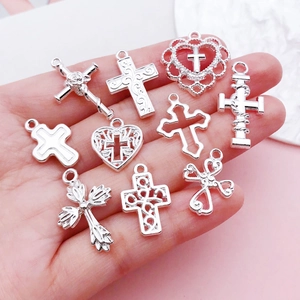 Set of 10 silver alloy cross and heart pendants held in palm showing scale and variety