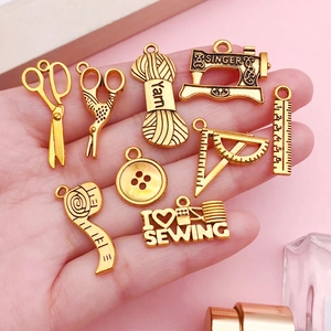 Close-up of golden vintage sewing machine charms held by hand against a pink background