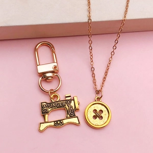 Antique gold sewing machine and button pendant set on minimalist pink background
