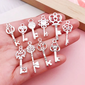 Close-up of ten vintage silver wing and heart key charms held in a hand for DIY jewelry
