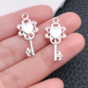 Macro shot of silver wing heart key pendants with vintage scrollwork details on hand
