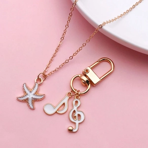 White enamel starfish necklace and music note keychain set on a soft pink background
