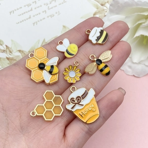 Détail de breloques émaillées abeille et tournesol en main pour bijoux artisanaux