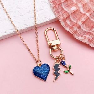 Collana oro rosa con cuore glitter blu scuro e ciondoli smaltati su sfondo rosa pastello