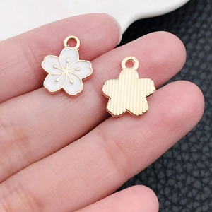 Macro shot of white and gold cherry blossom charms held on fingers for size detail