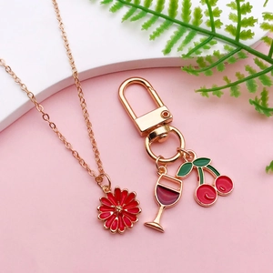 Detail view of red cherry and flower charms on golden alloy keychain and necklace