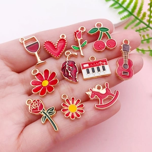 Macro view of assorted red enamel DIY charms including cherry and flower shapes in hand