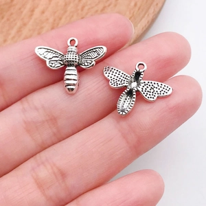 Detail view of bee charms showing front wing texture and reverse side on a hand