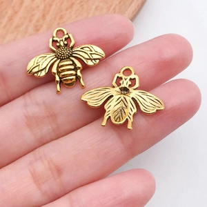 Close-up of two small bee-shaped metal pendants with antique gold finish on fingertips