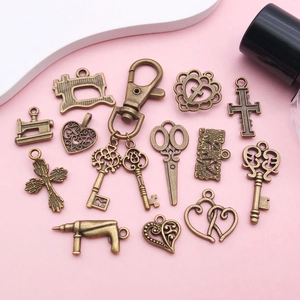 Detail of vintage bronze alloy charms with scissor, heart, and cross shapes on pink background
