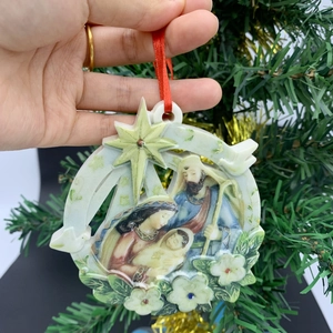 Detail of hand-held resin nativity ornament with gold star on a green Christmas tree
