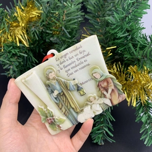 Holy Family Nativity scene hanging ornament with Spanish scripture on a Christmas tree