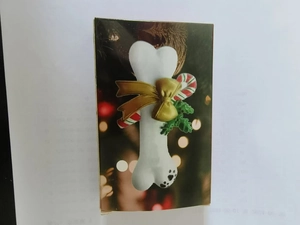 Packaged resin Christmas dog bone ornament with a festive bow and holly leaf detail