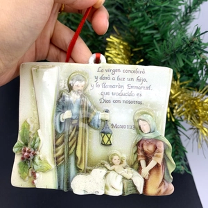 Detail of hand-held ceramic nativity scene ornament with biblical verse and red ribbon