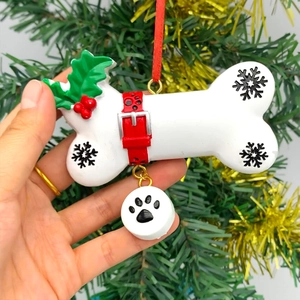 Christmas tree dog bone ornament with red ribbon and paw print tag in hand