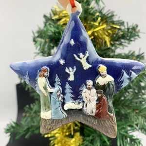 Detail of star-shaped resin nativity ornament hanging on a festive Christmas tree branch