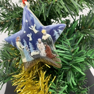 Detailed view of nativity scene star ornament hanging on a festive Christmas tree branch