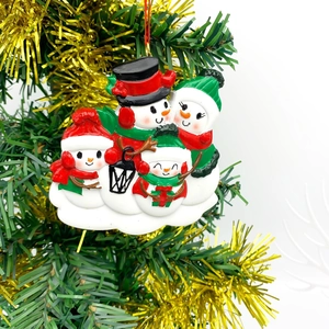 Détail d'un ornement de famille de 4 bonhommes de neige en résine sur un sapin