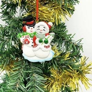Resin snowman couple Christmas ornament hanging on tree branch with festive red gift box