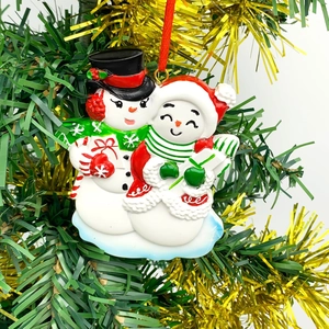 Detail of resin snowman couple ornament with gift box on a Christmas tree branch