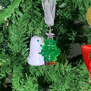 Close-up of green resin tree ornament and white bell hanging on Christmas tree branch