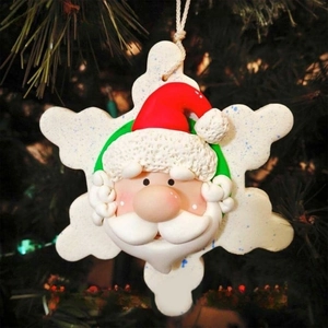 Detail of resin Santa Claus snowflake ornament hanging on a Christmas tree with warm lights