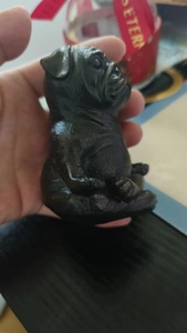 Detailed close-up of a meditating black pug resin statue in a yoga pose held in hand