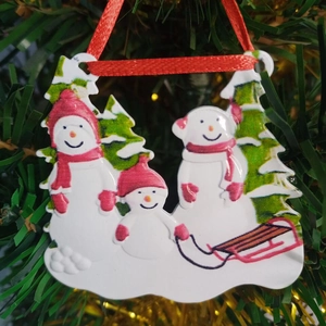 Close-up of resin snowman family ornament hanging on a Christmas tree with red ribbon
