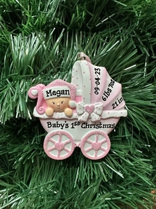 Close-up of pink personalized baby's first Christmas stroller ornament on a green tree