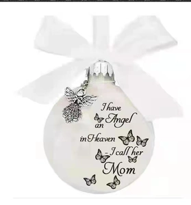 Close-up of white memorial ornament ball with Mom text, ribbon, and angel charm