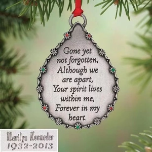 Silver teardrop Christmas ornament with floral relief and gemstones on a tree branch