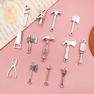 Flat lay of 12 silver alloy mini tool charms including hammer and saw on pink backdrop