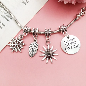 Silver snake chain bracelet with snowflake leaf and motivational quote charms on pink background