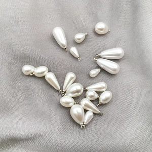 Macro shot of white teardrop pearl charms with gold loops on grey mesh background