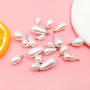Flat lay of teardrop pearl pendants with silver metal clasps on a pink background