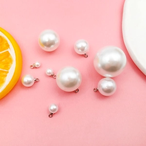 Primer plano de colgantes de perlas blancas redondas con tapas de plata sobre fondo rosa